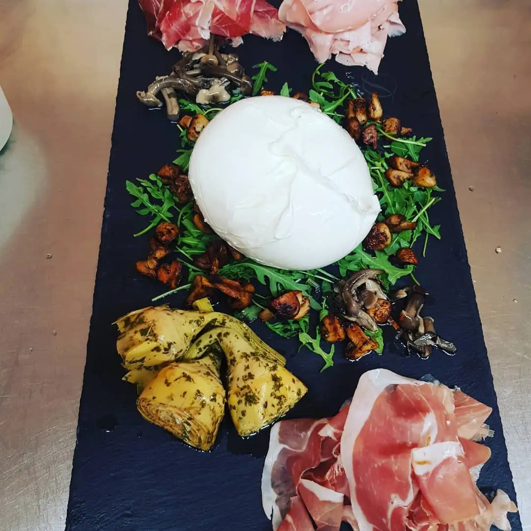 Burrata mit Rohschinken, Rucola und eingelegtem Gemüse auf der Schieferplatte